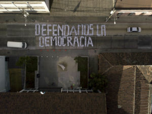 In this Jan. 9, 2019 photo, seen from above, a sign covering a street forms the Spanish phrase: "We defend democracy," made with photographs of the president and his cabinet